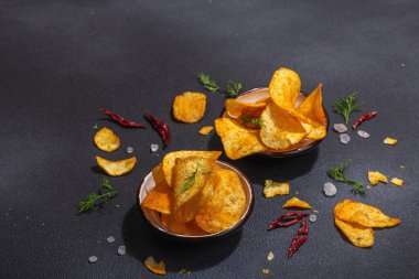 Kırmızı biber, maydanoz ve siyah beton arka planda tuz ile servis edilen ev yapımı patates cipsi kaseleri. Moda sabit ışık, karanlık gölge, boşluğu kopyala