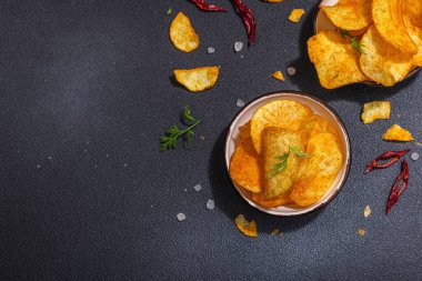 Kırmızı biber, maydanoz ve siyah beton arka planda tuz ile servis edilen ev yapımı patates cipsi kaseleri. Modaya uygun sert ışık, koyu gölge, üst manzara