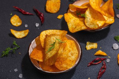 Kırmızı biber, maydanoz ve siyah beton arka planda tuz ile servis edilen ev yapımı patates cipsi kaseleri. Modaya uygun sert ışık, karanlık gölge, yaklaş