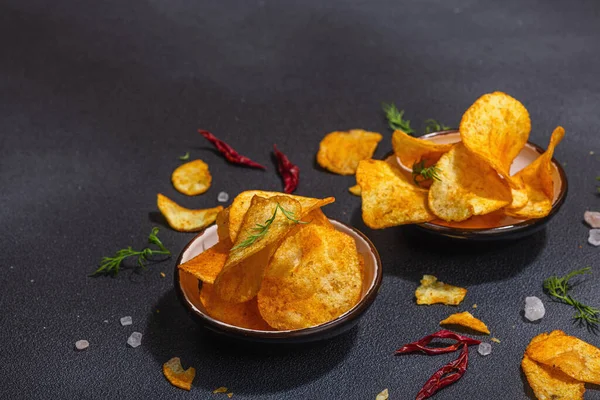 Kırmızı biber, maydanoz ve siyah beton arka planda tuz ile servis edilen ev yapımı patates cipsi kaseleri. Moda sabit ışık, karanlık gölge, boşluğu kopyala