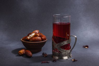 Hibiscus sıcak çay ve hurma. Koyu beton zeminde iftar ya da Suhoor yemeği için geleneksel Ramazan Kareem konsepti. Arap tatlısı, sert ışık, karanlık gölge, kopyalama alanı.