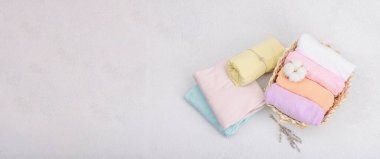 Giysilerin dikey depolanması. Bahar dolabı temizliği, çevre dostu hasır sepet. Pastel renkli bebek tişörtleri, makine yıkadıktan sonra katlanmış. Hafif taş arkaplan, pankart biçimi