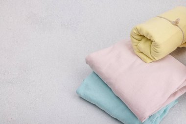 Giysilerin dikey depolanması. Bahar dolabı temizliği, çevre dostu hasır sepet. Pastel renkli bebek tişörtleri, makine yıkadıktan sonra katlanmış. Hafif taş arkaplan, boşluğu kopyala