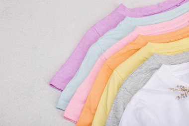 Giysilerin dikey depolanması. Çevre dostu bahar tuvaleti temizliği. Pastel renkli bebek tişörtleri, satış konsepti. Hafif taş arkaplan, üst görünüm