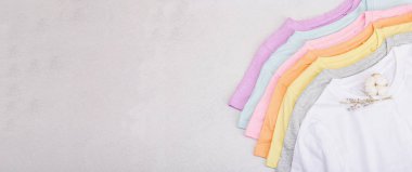Giysilerin dikey depolanması. Çevre dostu bahar tuvaleti temizliği. Pastel renkli bebek tişörtleri, satış konsepti. Hafif taş arkaplan, pankart biçimi