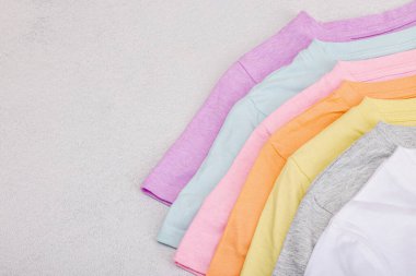Giysilerin dikey depolanması. Çevre dostu bahar tuvaleti temizliği. Pastel renkli bebek tişörtleri, satış konsepti. Hafif taş arkaplan, üst görünüm