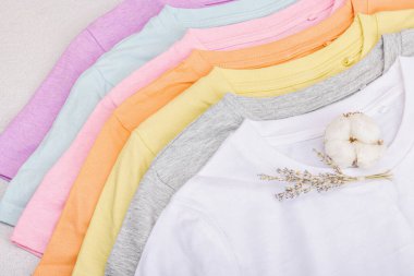 Giysilerin dikey depolanması. Çevre dostu bahar tuvaleti temizliği. Pastel renkli bebek tişörtleri, satış konsepti. Hafif taş arkaplan, üst görünüm