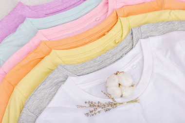 Giysilerin dikey depolanması. Çevre dostu bahar tuvaleti temizliği. Pastel renkli bebek tişörtleri, satış konsepti. Hafif taş arkaplan, üst görünüm