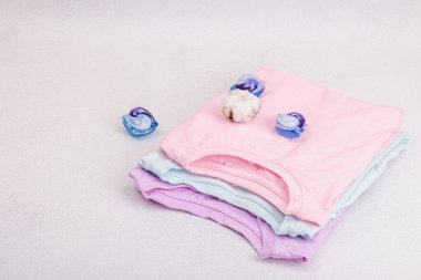 Eko dostu bahar tuvaleti temizliği, makine yıkama kapsülleri. Pastel renkli bebek tişörtleri, satış konsepti. Giysilerin dikey depolanması. Hafif taş arkaplan, boşluğu kopyala