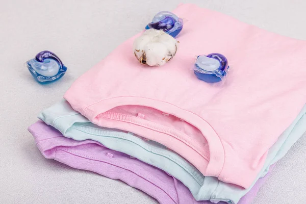 stock image Eco friendly spring closet cleaning, capsules for machine washing. Pastel colored baby T-shirts, sale concept. Vertical storage of clothing. Light stone concrete background, close up