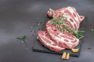 Çiğ domuz eti. Biftek, kırmızı biber, sarımsaklı karanfil, deniz tuzu ve taze biberiye. Moda standı, siyah arkaplan, düz yatış, kopyalama alanı