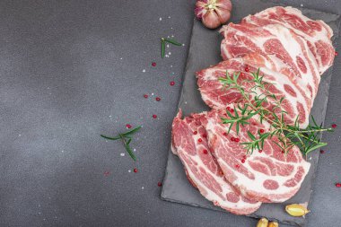 Çiğ domuz eti. Biftek, kırmızı biber, sarımsaklı karanfil, deniz tuzu ve taze biberiye. Moda standı, siyah arkaplan, düz konum, üst görünüm