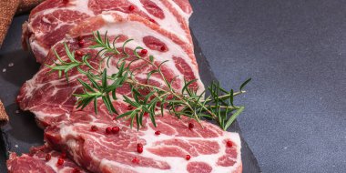 Çiğ domuz eti. Biftek, kırmızı biber, sarımsaklı karanfil, deniz tuzu ve taze biberiye. Moda duruşu, siyah arkaplan, düz yatış, pankart biçimi