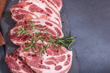 Çiğ domuz eti. Biftek, kırmızı biber, sarımsaklı karanfil, deniz tuzu ve taze biberiye. Moda standı, siyah arkaplan, düz konum, üst görünüm