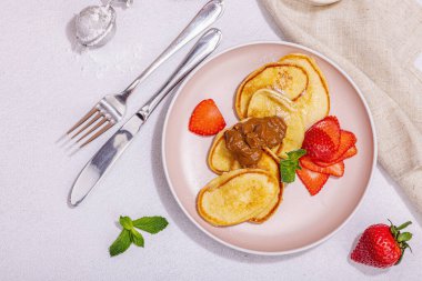 Süzme peynirli krep, şurup, çilekli krep, pembe tabakta nane ve pudra şekeri. Seçici odaklanma, lezzetli kahvaltı. Modaya uygun beton zemin, üst görünüm