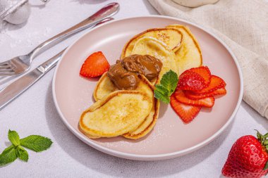 Süzme peynirli krep, şurup, çilekli krep, pembe tabakta nane ve pudra şekeri. Seçici odaklanma, lezzetli kahvaltı. Modaya uygun beton arka plan, kapat