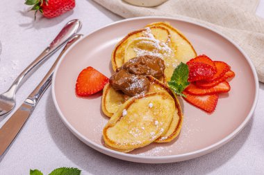 Süzme peynirli krep, şurup, çilekli krep, pembe tabakta nane ve pudra şekeri. Seçici odaklanma, lezzetli kahvaltı. Modaya uygun beton arka plan, kapat