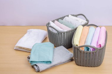 Sepetlerde dikey giysi deposu var. Bahar tuvaleti temizliği, çevre dostu tarzı. Pastel renkli bebek tişörtleri, makine yıkadıktan sonra katlanmış. Hafif ahşap masa, boşluğu kopyala