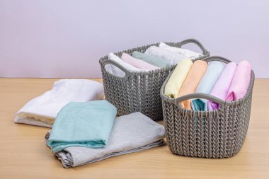 Sepetlerde dikey giysi deposu var. Bahar tuvaleti temizliği, çevre dostu tarzı. Pastel renkli bebek tişörtleri, makine yıkadıktan sonra katlanmış. Hafif ahşap masa, boşluğu kopyala