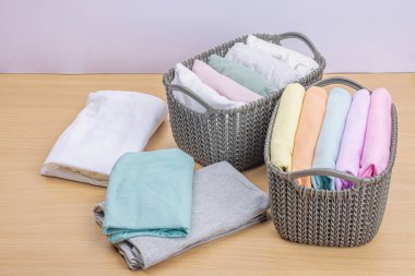Sepetlerde dikey giysi deposu var. Bahar tuvaleti temizliği, çevre dostu tarzı. Pastel renkli bebek tişörtleri, makine yıkadıktan sonra katlanmış. Hafif ahşap masa, boşluğu kopyala