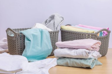 Sepetlerde dikey giysi deposu var. Bahar tuvaleti temizliği, çevre dostu tarzı. Pastel renkli bebek tişörtleri, makine yıkadıktan sonra katlanmış. Hafif ahşap masa, boşluğu kopyala