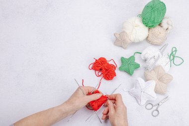 Kadınların elleri yeni yıl süslerini örgü iğneleriyle örer. Yumuşak, şehvetli yıldızlar, iplikler, aksesuarlar. Hobi, el yapımı konsept. Işık taşı arkaplan, düz yatış, üst görünüm