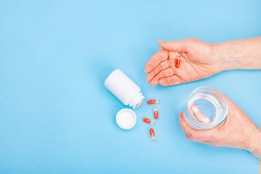 Bir kadın ilaç alır. Kadın eli kapsül ya da hap tutar. Tedavi, vitamin almak, sağlık hizmeti kavramı. Mavi arkaplan, düz yatış, üst görünüm