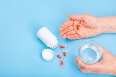 Bir kadın ilaç alır. Kadın eli kapsül ya da hap tutar. Tedavi, vitamin almak, sağlık hizmeti kavramı. Mavi arkaplan, düz yatış, üst görünüm