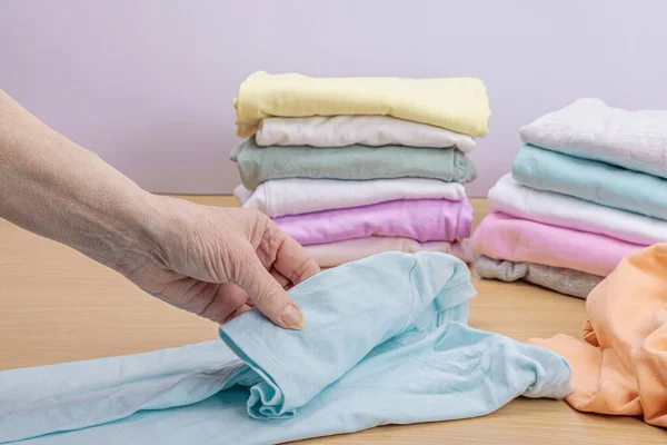 stock image Women's hands fold clean clothes. Vertical storage of clothing in the baskets. Closet cleaning, eco friendly style. Pastel colored baby T-shirts. Light wooden table, copy space