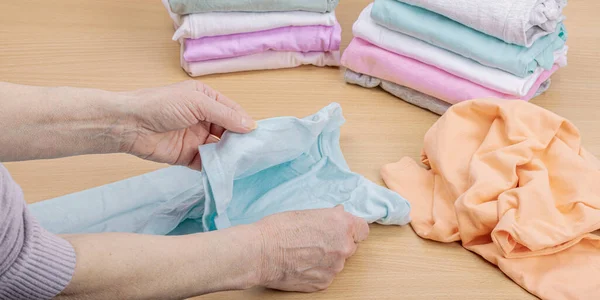 stock image Women's hands fold clean clothes. Vertical storage of clothing in the baskets. Closet cleaning, eco friendly style. Pastel colored baby T-shirts. Light wooden table, copy space