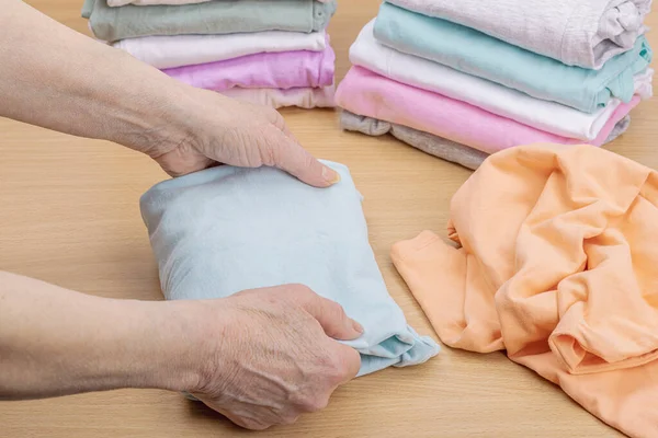 stock image Women's hands fold clean clothes. Vertical storage of clothing in the baskets. Closet cleaning, eco friendly style. Pastel colored baby T-shirts. Light wooden table, copy space