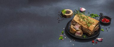 Baharatla pişirilmiş tuzlu, yüksek yağlı et parçaları. Salo, pastırma, domuz yağı, gümüş, tavla. Sarımsak, taze defne yaprağı, biberiye, baharat, biber. Siyah taş arkaplan, pankart biçimi