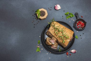 Baharatla pişirilmiş tuzlu, yüksek yağlı et parçaları. Salo, pastırma, domuz yağı, gümüş, tavla. Sarımsak, taze defne yaprağı, biberiye, baharat, biber. Siyah taş arkaplan, üst görünüm