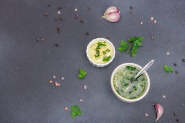 Salata sosu. Krema sosu ve baharatlı sarımsak yağı ve taze yeşillikler. Mutfak arka planı, siyah taş beton, düz döşeme, üst manzara