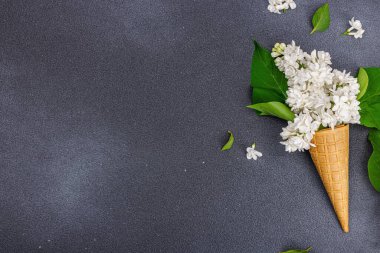 Koyu taş arkaplanda kremalı dondurma külahında beyaz leylak çiçekleri. Düz yatak, geleneksel bahar konsepti, üst manzara