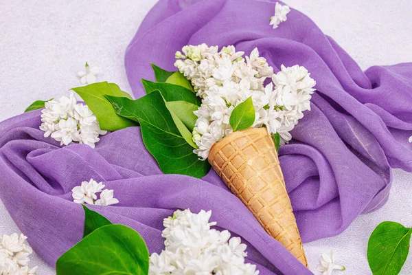 白色紫丁香花在华夫饼冰淇淋锥上的轻石料混凝土背景 紫色餐巾 传统的春天观念 — 图库照片