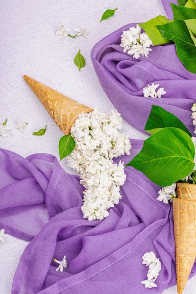 白色紫丁香花在华夫饼冰淇淋锥上的轻石料混凝土背景 紫色餐巾 传统的春天观念 顶视图 — 图库照片