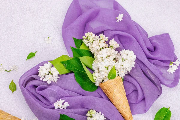 白色紫丁香花在华夫饼冰淇淋锥上的轻石料混凝土背景 紫色餐巾 传统的春天观念 顶视图 — 图库照片
