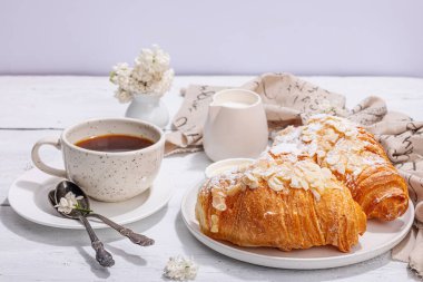 Günaydın konsepti. Bir fincan kahve ve taze kruvasanla kahvaltı. Tatlı kremalı sos, sert ışık, koyu gölge. Beyaz tahta arkaplan, boşluğu kopyala