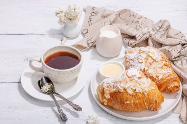 Günaydın konsepti. Bir fincan kahve ve taze kruvasanla kahvaltı. Tatlı kremalı sos, sert ışık, koyu gölge. Beyaz tahta arkaplan, boşluğu kopyala