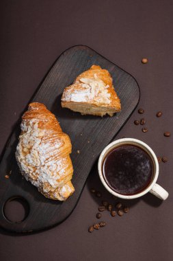 Günaydın konsepti. Bir fincan kahve ve taze kruvasanla kahvaltı. Tatlı kremalı sos, sert ışık, koyu gölge. Kahverengi arkaplan, yapısal bozulma, seçici odak, üst görünüm