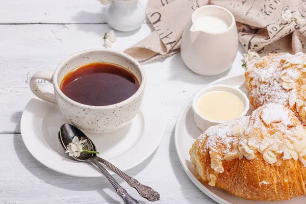 stock image Good morning concept. Breakfast with cup of coffee and fresh croissant. Sweet creamy sauce, hard light, dark shadow. White wooden background, close up