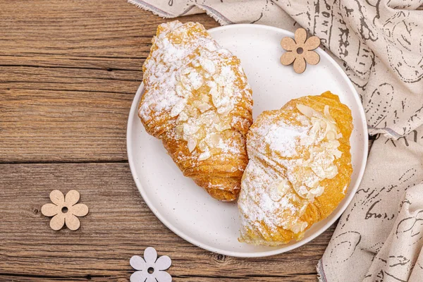 Good morning concept. Fresh croissants with cream filling and almond flakes. Sweet dessert, wooden background, top view