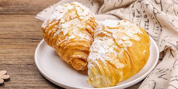 Good morning concept. Fresh croissants with cream filling and almond flakes. Sweet dessert, wooden background, banner format