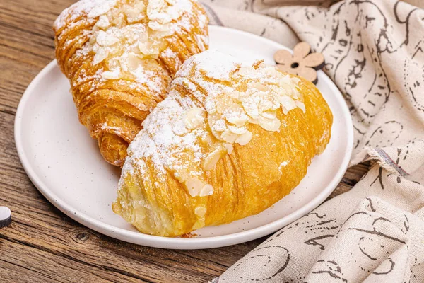 Good morning concept. Fresh croissants with cream filling and almond flakes. Sweet dessert, wooden background, close up