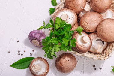 Ham kahverengi kraliyet şampiyonları sepette. Vejetaryen yemekleri pişirmek. Sarımsak, yeşillik, baharat, sert ışık, koyu gölge. Yenilebilir mantarlar, modern bir eğilim, beyaz arka plan, üst görünüm