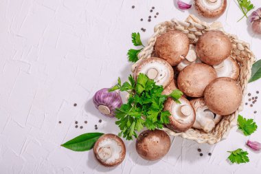 Ham kahverengi kraliyet şampiyonları sepette. Vejetaryen yemekleri pişirmek. Sarımsak, yeşillik, baharat, sert ışık, koyu gölge. Yenilebilir mantarlar, modern bir eğilim, beyaz arka plan, üst görünüm