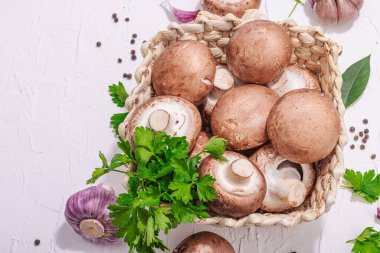 Ham kahverengi kraliyet şampiyonları sepette. Vejetaryen yemekleri pişirmek. Sarımsak, yeşillik, baharat, sert ışık, koyu gölge. Yenilebilir mantarlar, modern bir eğilim, beyaz arka plan, üst görünüm