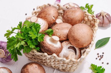 Ham kahverengi kraliyet şampiyonları sepette. Vejetaryen yemekleri pişirmek. Sarımsak, yeşillik, baharat, sert ışık, koyu gölge. Yenilebilir mantarlar, modern trend, beyaz arkaplan, kapat