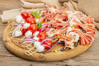 Şişe üzerinde piknik atıştırmalıkları. Jamon, mozzarella, kiraz domatesleri, bezelyeler, taze yeşiller. Modern duruş, ahşap zemin, yakın plan.